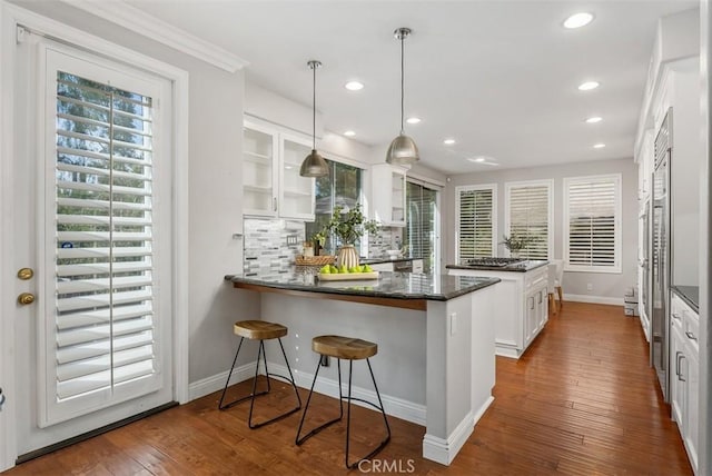 kitchen featuring backsplash, dark wood-style floors, a peninsula, white cabinets, and glass insert cabinets