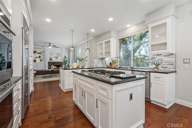 kitchen with glass insert cabinets, ceiling fan, dark wood-type flooring, a lit fireplace, and stainless steel appliances