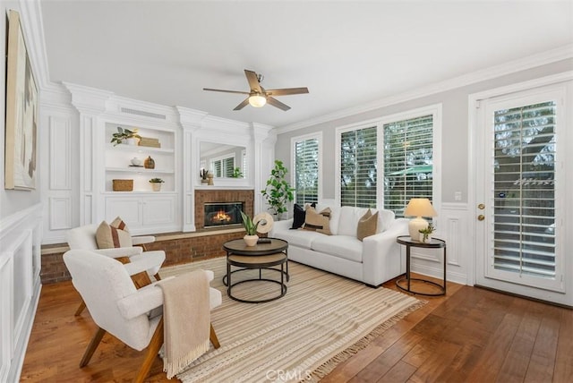 living room with hardwood / wood-style floors, built in features, ornamental molding, a brick fireplace, and a decorative wall