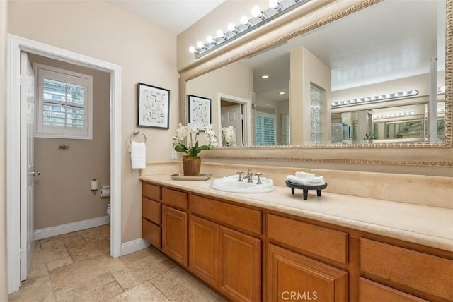 bathroom with stone tile flooring, toilet, vanity, and baseboards