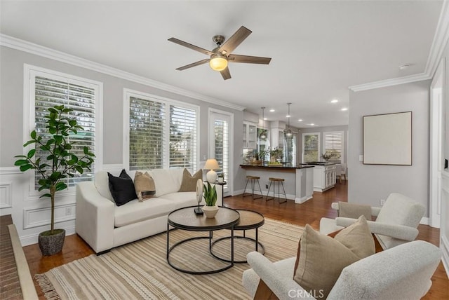 living area with a wealth of natural light, crown molding, a ceiling fan, and wood finished floors