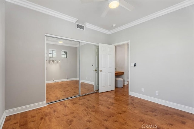 unfurnished bedroom featuring visible vents, baseboards, wood finished floors, and crown molding