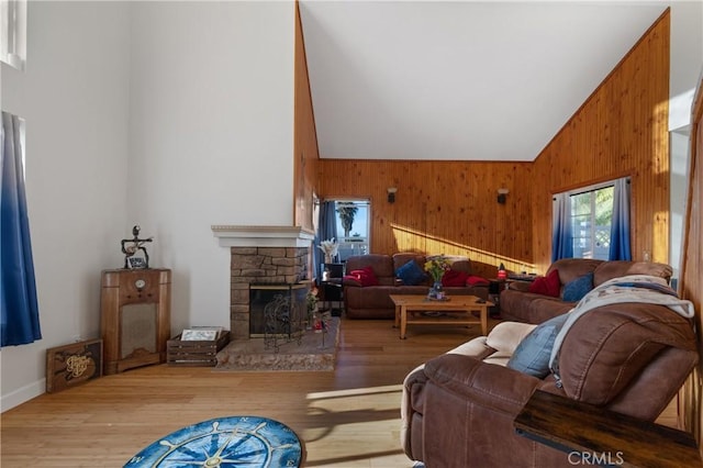 living room with light wood-type flooring, wood walls, a fireplace, and high vaulted ceiling