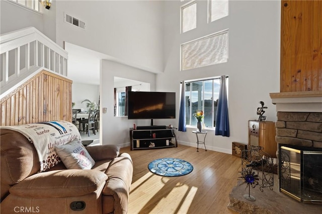 living room featuring visible vents, a towering ceiling, a stone fireplace, light wood-type flooring, and baseboards