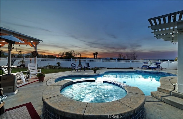 pool at dusk featuring a patio, a fenced backyard, and a pool with connected hot tub