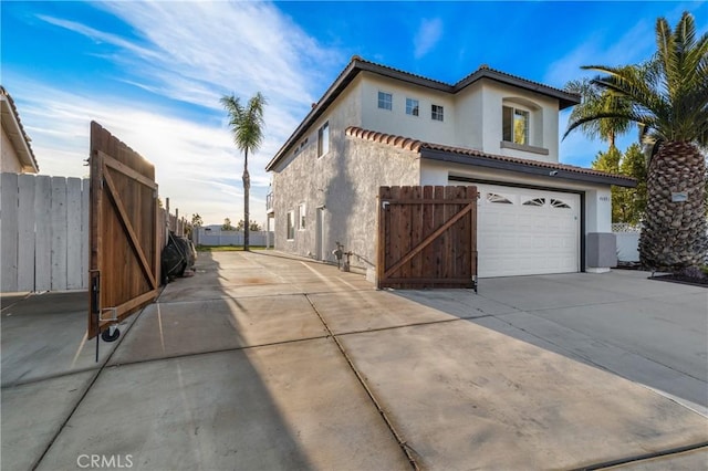 view of home's exterior featuring a tile roof, stucco siding, fence, a garage, and driveway