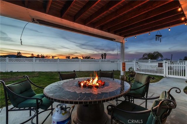 patio terrace at dusk with a yard, fence, and a fire pit