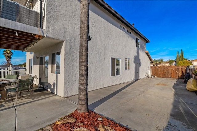 view of side of property featuring a patio, fence, a gate, and stucco siding