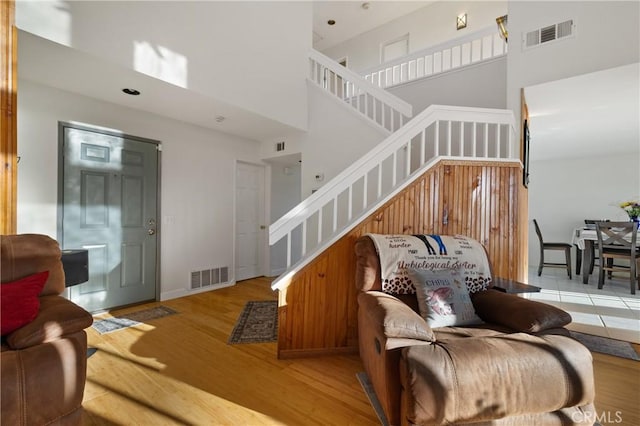 living area with stairs, light wood finished floors, a towering ceiling, and visible vents