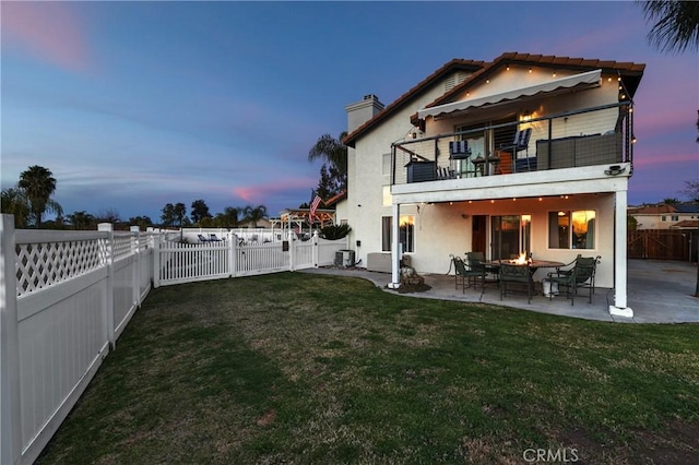 back of property at dusk with a fire pit, a balcony, a fenced backyard, a yard, and a patio area