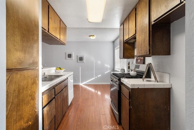 kitchen featuring sink, gas range, wood-type flooring, fridge, and white dishwasher