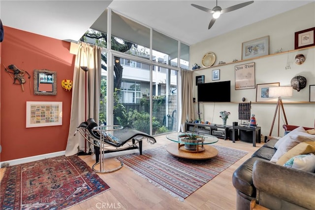 living room featuring ceiling fan, light wood-type flooring, and a wall of windows