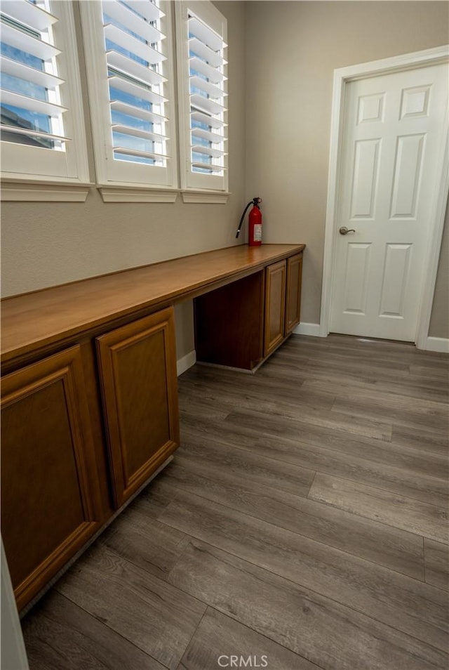 unfurnished office featuring dark wood-type flooring, built in study area, and baseboards