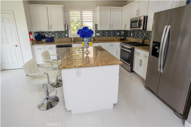 kitchen featuring white cabinets, a kitchen island, appliances with stainless steel finishes, light stone countertops, and light tile patterned flooring