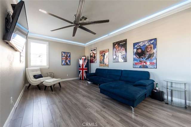 living area featuring a ceiling fan, ornamental molding, baseboards, and wood finished floors