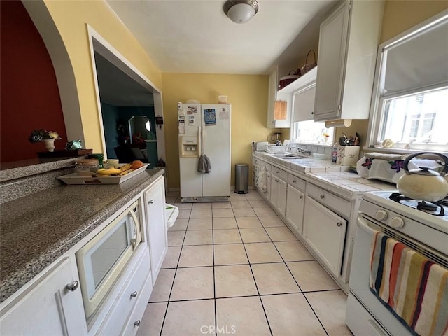 kitchen featuring light tile patterned flooring, sink, tile counters, white appliances, and white cabinets