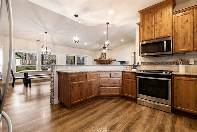 kitchen featuring lofted ceiling, stainless steel appliances, a peninsula, backsplash, and brown cabinetry