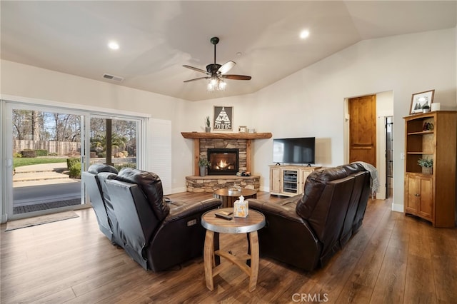 living room with visible vents, a ceiling fan, wood finished floors, vaulted ceiling, and a stone fireplace