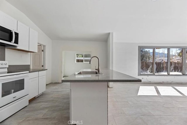 kitchen with dark countertops, white cabinets, an island with sink, white appliances, and a kitchen bar