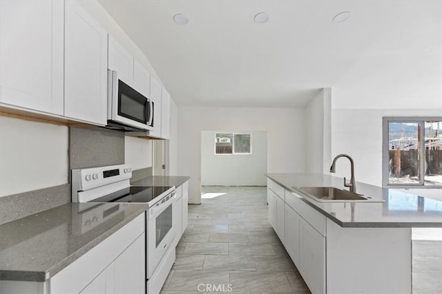 kitchen with white electric range oven, stainless steel microwave, white cabinetry, a sink, and an island with sink