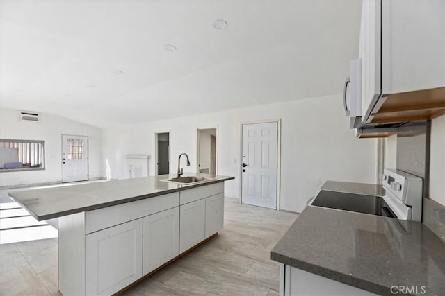 kitchen featuring a sink, white cabinetry, vaulted ceiling, range, and a center island with sink