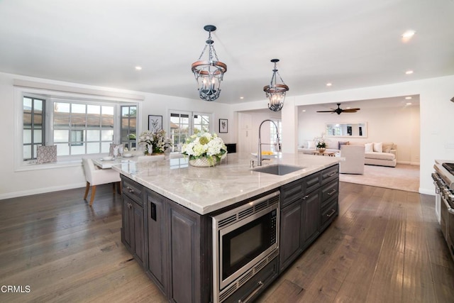 kitchen featuring sink, stainless steel microwave, hanging light fixtures, an island with sink, and light stone countertops