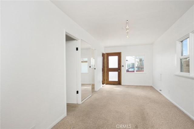 spare room featuring light carpet, a wealth of natural light, and baseboards