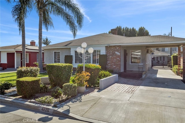 ranch-style home featuring brick siding, an attached carport, concrete driveway, and a gate