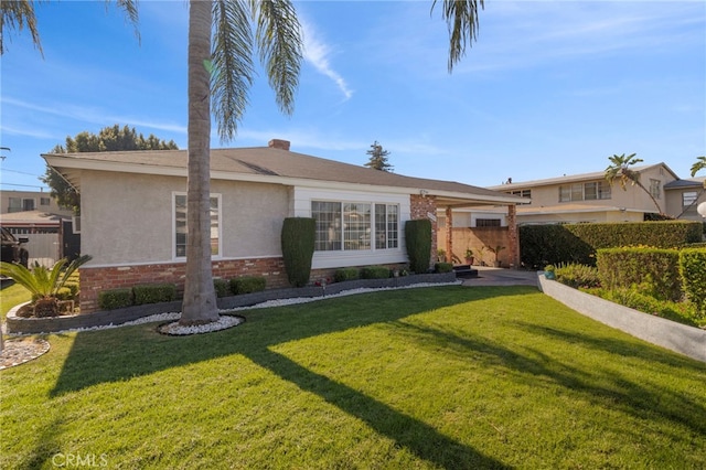 single story home featuring a front yard, a chimney, brick siding, and stucco siding