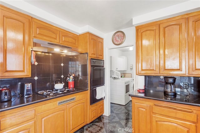 kitchen featuring dobule oven black, under cabinet range hood, gas cooktop, dark countertops, and washer / dryer