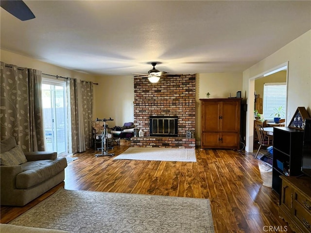 living room with dark wood-type flooring, a brick fireplace, and ceiling fan