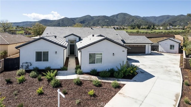 view of front of home with driveway, a mountain view, stucco siding, and fence