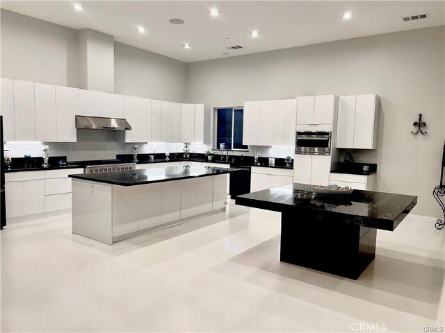 kitchen featuring a high ceiling, dark countertops, stainless steel oven, a kitchen island, and extractor fan