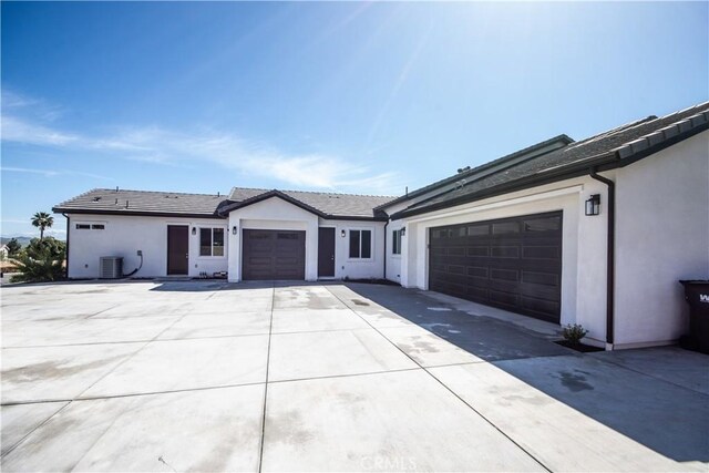 view of front of home with concrete driveway, central air condition unit, stucco siding, and an attached garage