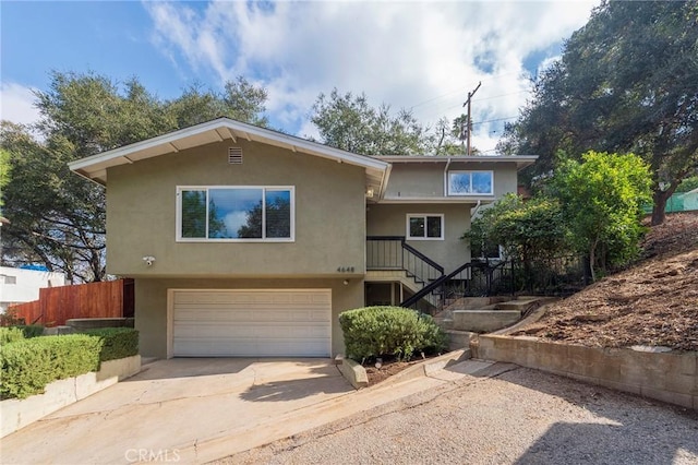 view of front of property featuring driveway, fence, an attached garage, and stucco siding