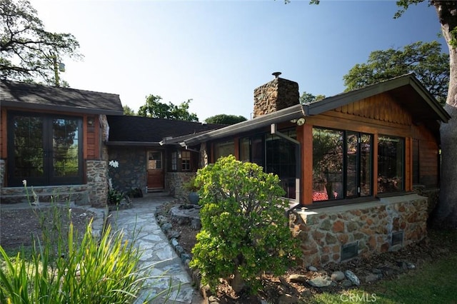 back of property featuring stone siding, french doors, a chimney, and a sunroom