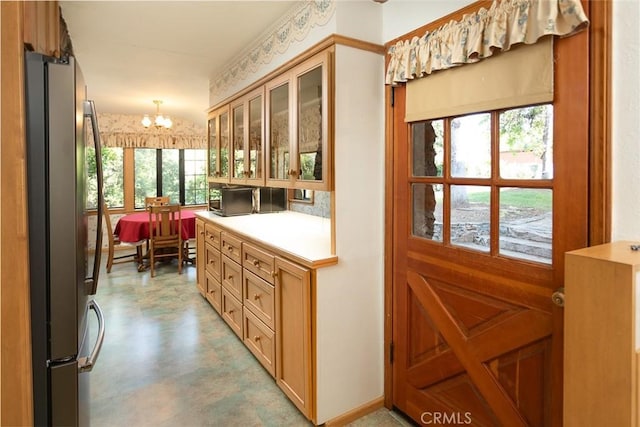 kitchen featuring pendant lighting, light countertops, freestanding refrigerator, glass insert cabinets, and an inviting chandelier