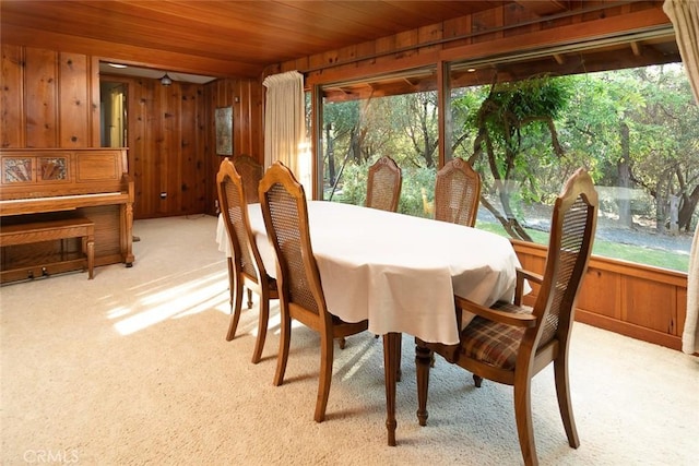 dining area with wood ceiling, light carpet, and wooden walls