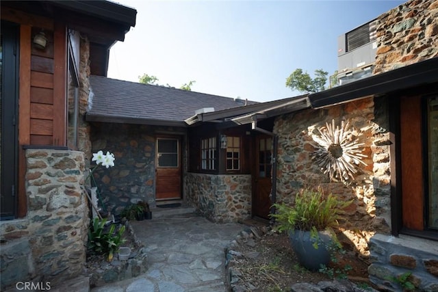 entrance to property with stone siding and roof with shingles