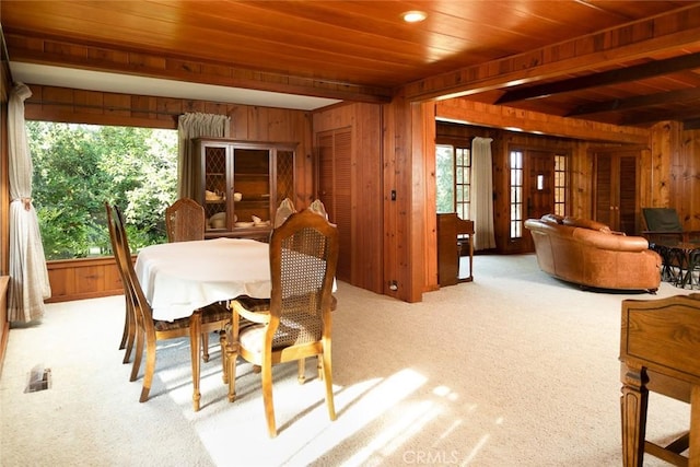 dining space with wooden walls, beamed ceiling, and light colored carpet