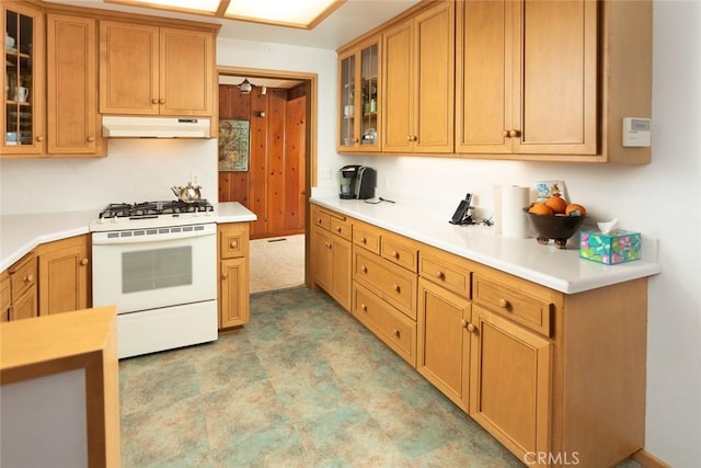 kitchen with light countertops, white gas range, glass insert cabinets, and under cabinet range hood