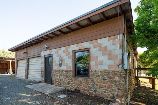 rear view of property featuring a garage and stone siding