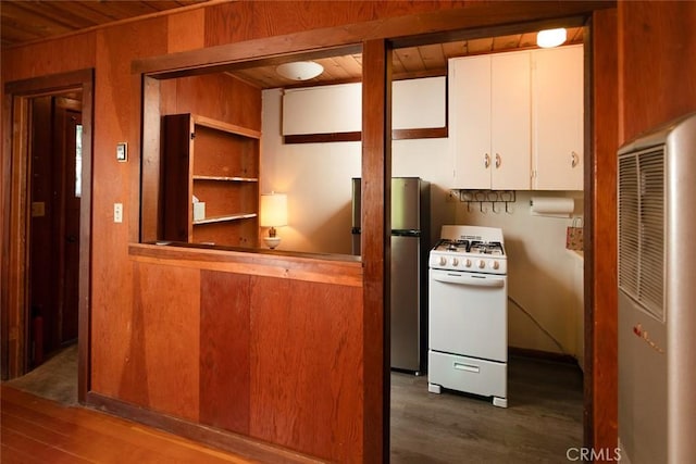 kitchen with white range with gas cooktop, white cabinets, dark wood-type flooring, freestanding refrigerator, and wood walls