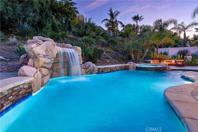 pool at dusk with a pool with connected hot tub and fence