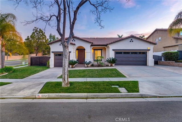 mediterranean / spanish home with a garage, fence, concrete driveway, a lawn, and stucco siding