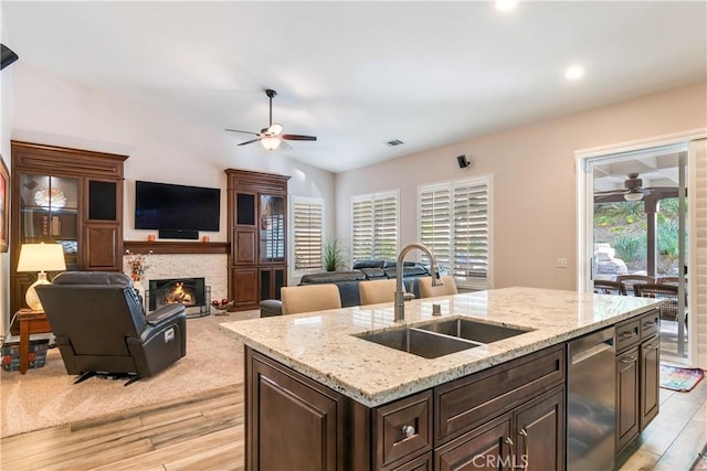 kitchen featuring a sink, open floor plan, light stone countertops, dishwasher, and an island with sink