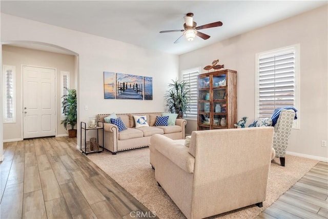 living area featuring light wood-style floors, arched walkways, baseboards, and a ceiling fan