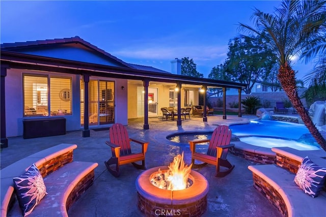 exterior space with stucco siding, a patio area, a fire pit, and an in ground hot tub