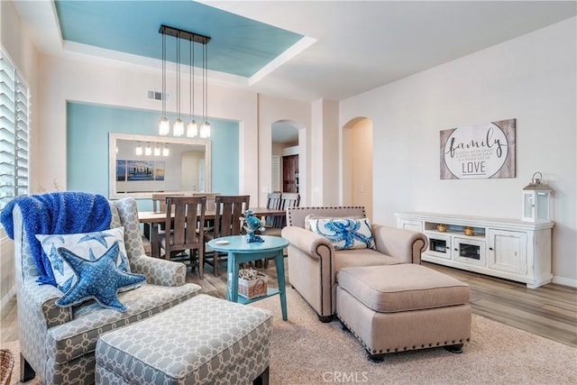 living area with arched walkways, a tray ceiling, wood finished floors, and visible vents