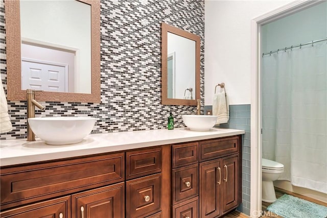 bathroom with double vanity, a sink, toilet, and tile walls